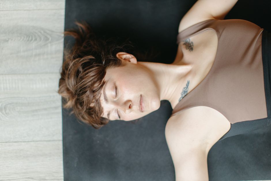 Woman lying on a yoga mat indoors with eyes closed, conveying relaxation.